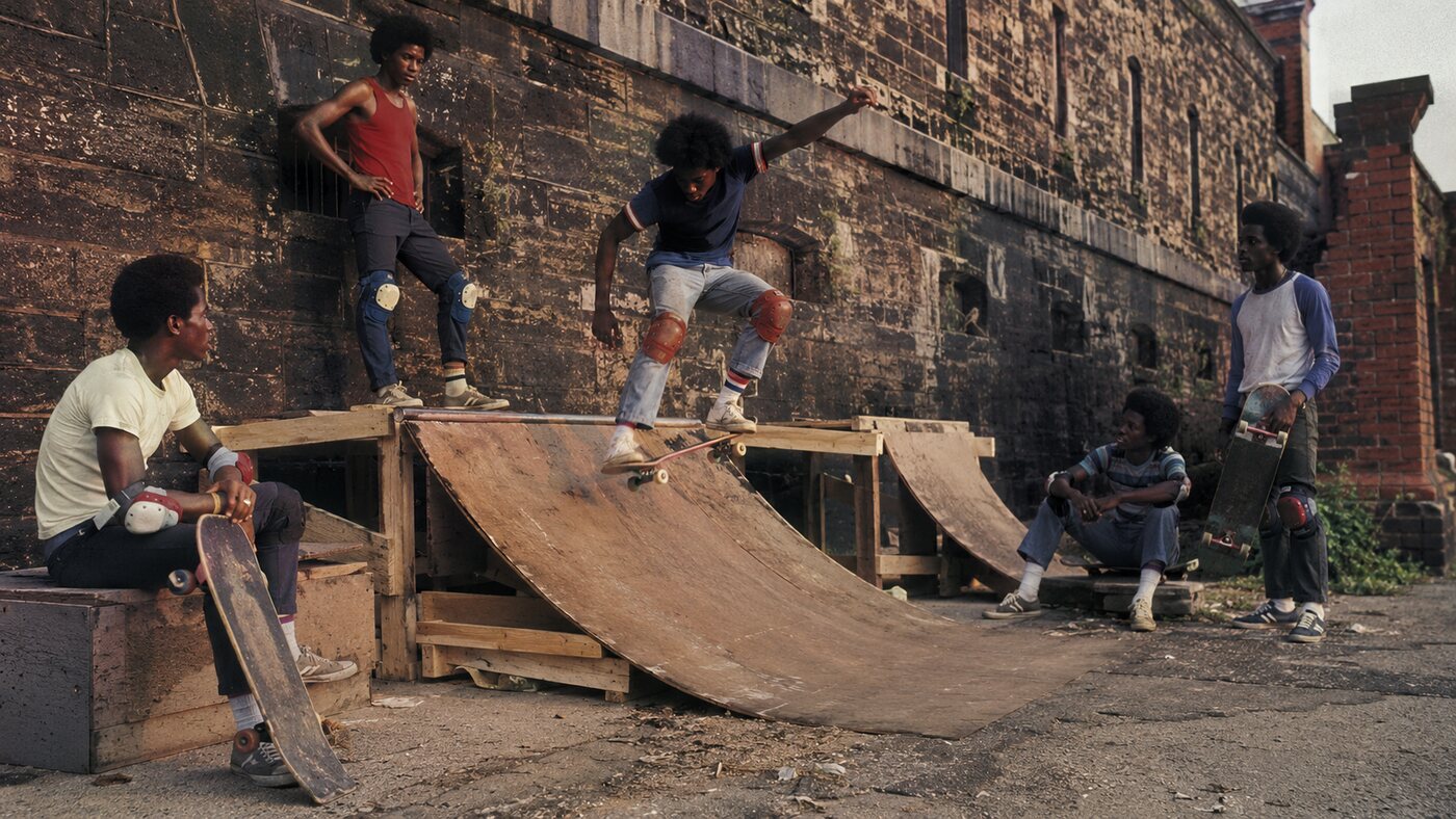 Young Black skateboarders gathered around a handmade ramp in an archival-style scene